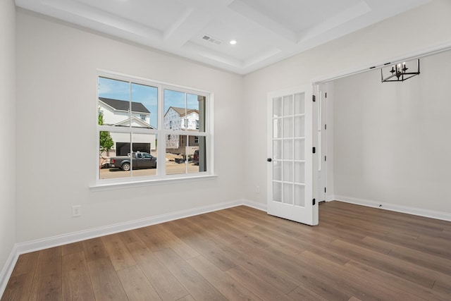 spare room featuring beamed ceiling, wood-type flooring, coffered ceiling, and an inviting chandelier