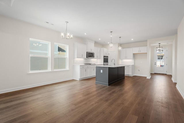 kitchen featuring appliances with stainless steel finishes, white cabinetry, a center island with sink, decorative light fixtures, and a chandelier