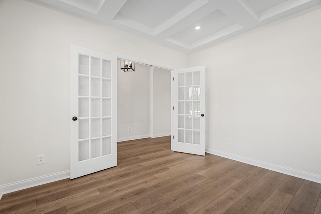 empty room with french doors, coffered ceiling, beamed ceiling, a chandelier, and hardwood / wood-style flooring