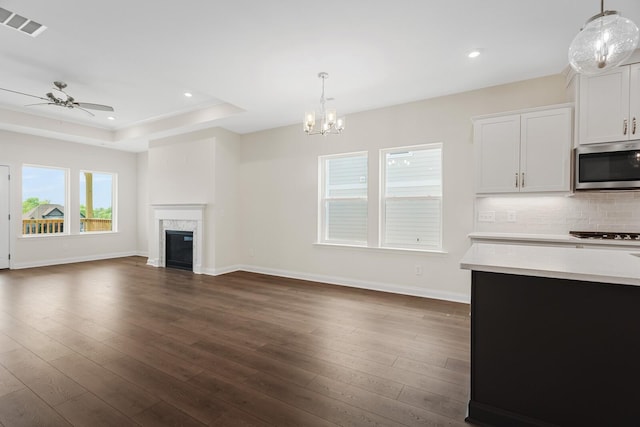 unfurnished living room featuring dark hardwood / wood-style flooring, a tray ceiling, and ceiling fan with notable chandelier