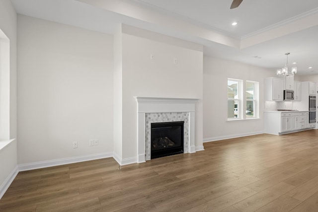 unfurnished living room with hardwood / wood-style flooring, a premium fireplace, ceiling fan with notable chandelier, and a tray ceiling