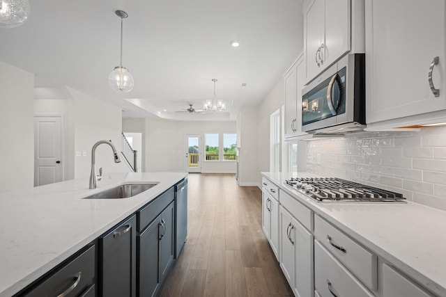 kitchen with appliances with stainless steel finishes, pendant lighting, white cabinetry, sink, and light stone counters