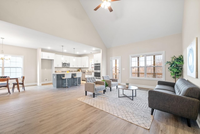 living room with ceiling fan with notable chandelier, high vaulted ceiling, and light hardwood / wood-style floors