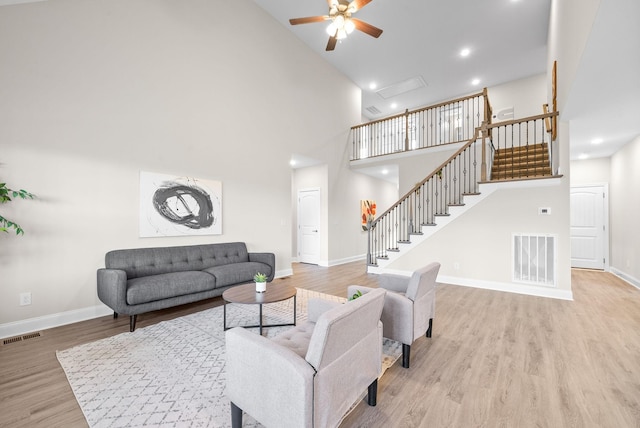 living room featuring ceiling fan, a high ceiling, and light wood-type flooring