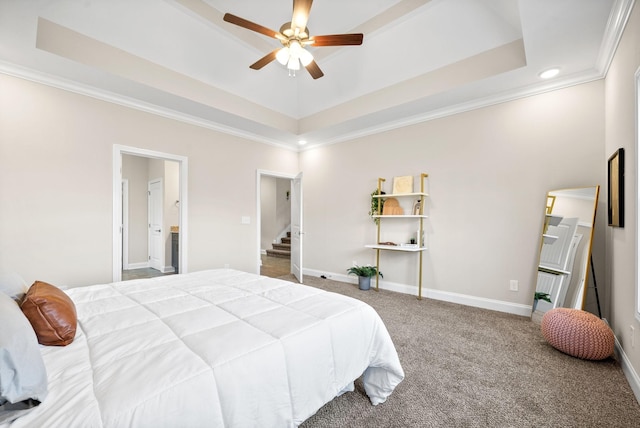 carpeted bedroom featuring a tray ceiling, ensuite bath, ornamental molding, and ceiling fan