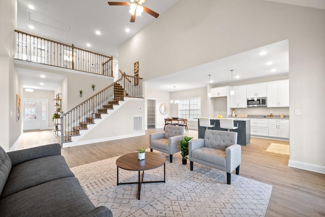 living room featuring a towering ceiling, ceiling fan with notable chandelier, and light wood-type flooring