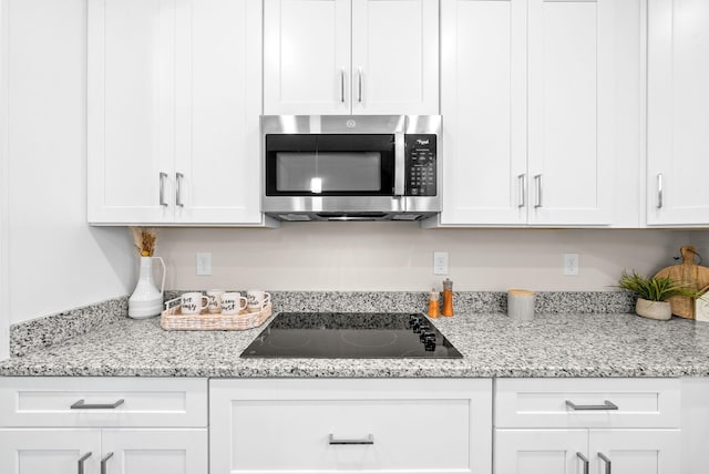 kitchen featuring black electric cooktop, light stone counters, and white cabinets