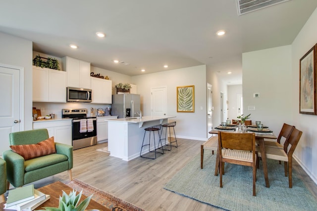 kitchen with appliances with stainless steel finishes, a breakfast bar area, white cabinets, light hardwood / wood-style floors, and a center island with sink