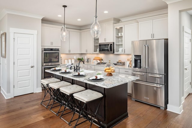 kitchen featuring white cabinetry, a kitchen breakfast bar, stainless steel appliances, light stone countertops, and a center island with sink