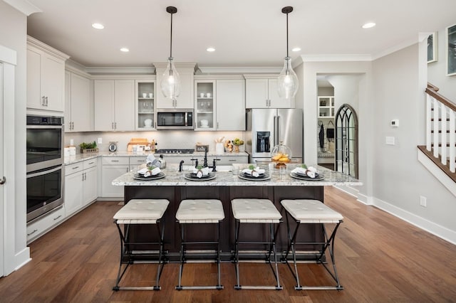 kitchen with pendant lighting, stainless steel appliances, light stone countertops, and a kitchen island with sink