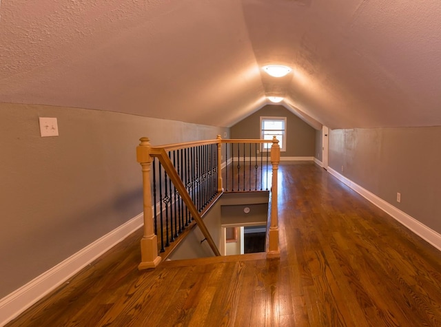 additional living space with dark wood-type flooring, vaulted ceiling, and a textured ceiling