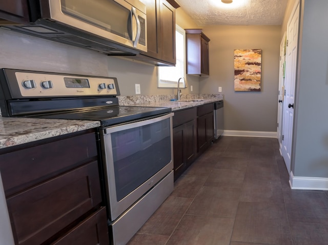 kitchen featuring dark brown cabinetry, sink, light stone counters, a textured ceiling, and appliances with stainless steel finishes