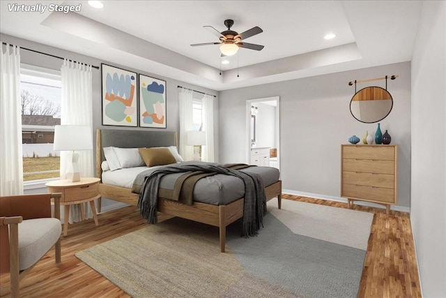 bedroom featuring hardwood / wood-style floors, a tray ceiling, ceiling fan, and ensuite bathroom