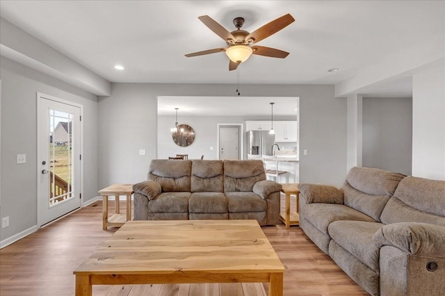 living room featuring sink, ceiling fan with notable chandelier, and light hardwood / wood-style flooring