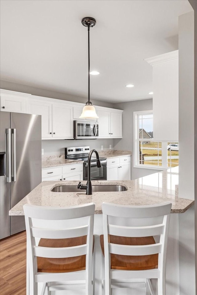 kitchen with pendant lighting, appliances with stainless steel finishes, a kitchen breakfast bar, and white cabinets