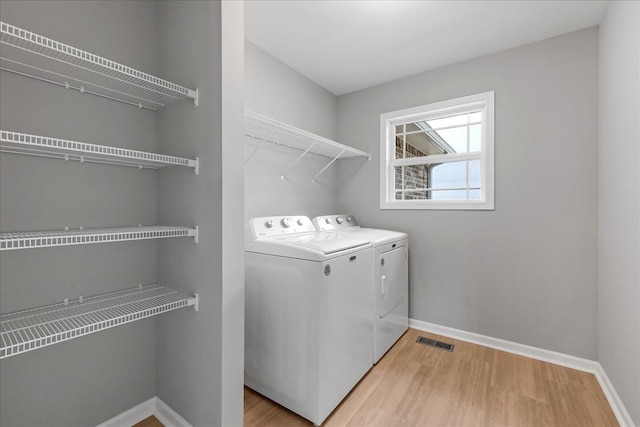 clothes washing area with washing machine and clothes dryer and light hardwood / wood-style flooring