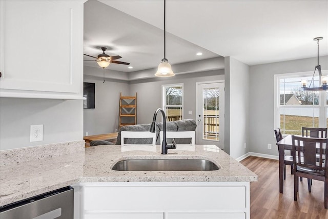 kitchen featuring light stone counters, hanging light fixtures, sink, and white cabinets