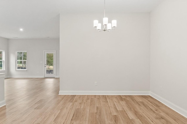 spare room with an inviting chandelier and light hardwood / wood-style floors