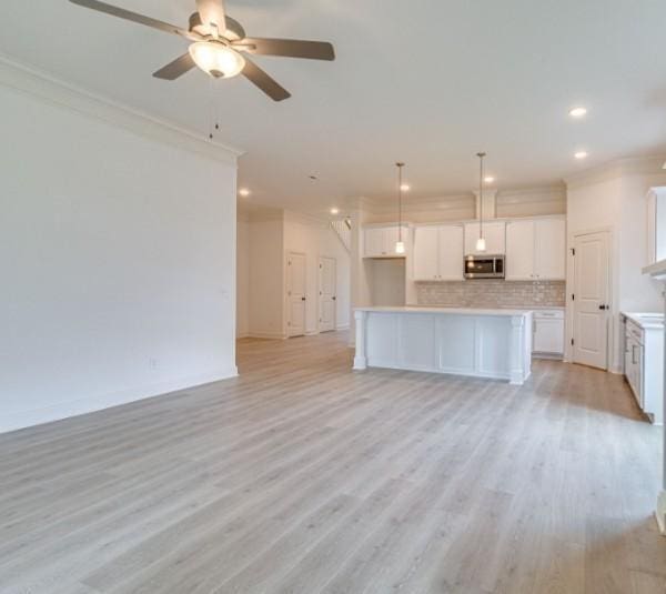 kitchen featuring decorative backsplash, decorative light fixtures, white cabinets, and a center island with sink