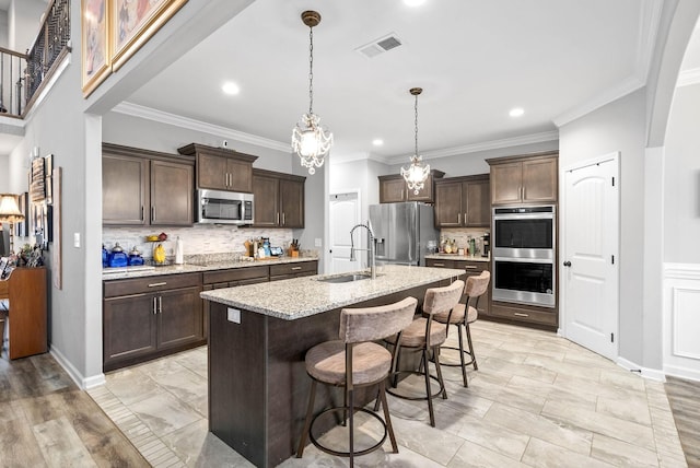 kitchen with dark brown cabinetry, sink, decorative light fixtures, appliances with stainless steel finishes, and an island with sink