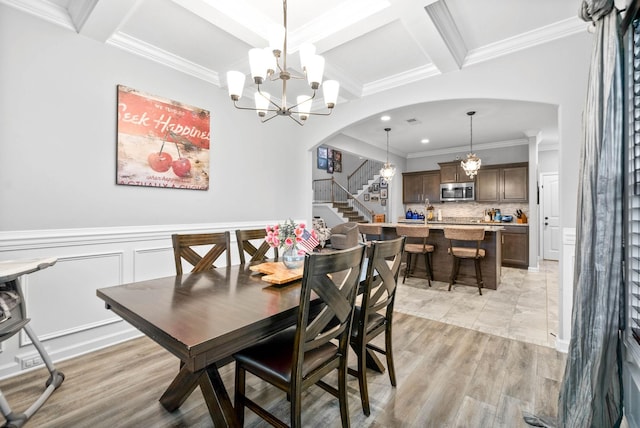 dining room with beamed ceiling, light wood-type flooring, ornamental molding, coffered ceiling, and an inviting chandelier