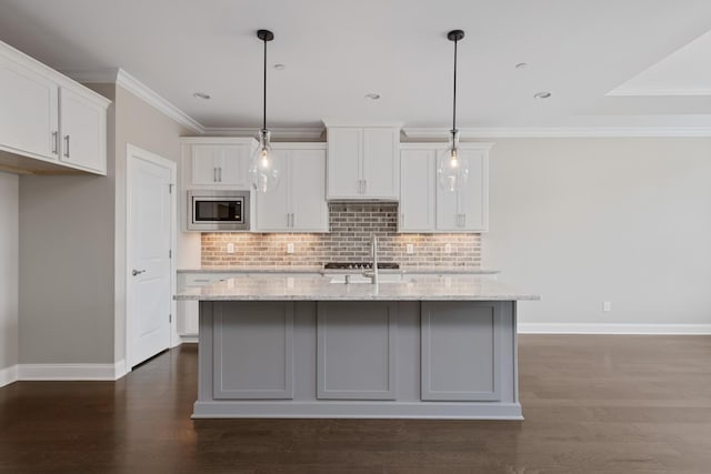 kitchen featuring stainless steel microwave, light stone countertops, white cabinets, and a center island with sink