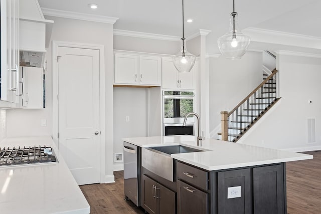 kitchen featuring dark wood-type flooring, appliances with stainless steel finishes, white cabinetry, hanging light fixtures, and a center island with sink