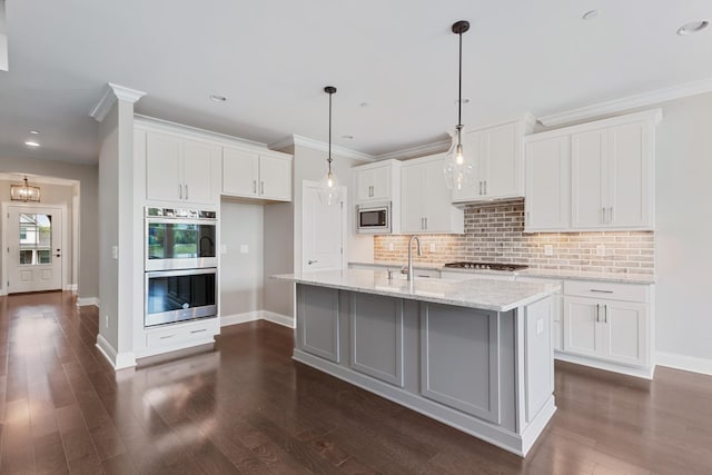 kitchen with white cabinets, hanging light fixtures, stainless steel appliances, light stone countertops, and a center island with sink