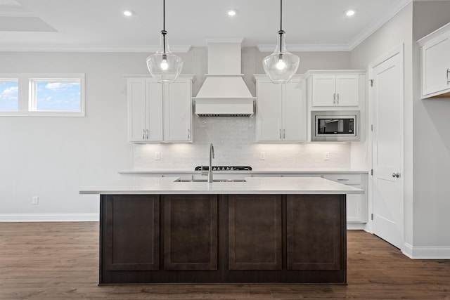 kitchen featuring stainless steel microwave, pendant lighting, custom exhaust hood, and white cabinets