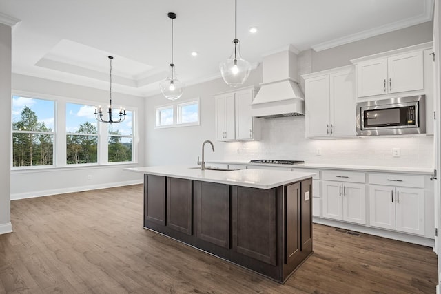 kitchen featuring stainless steel microwave, pendant lighting, sink, white cabinets, and custom range hood