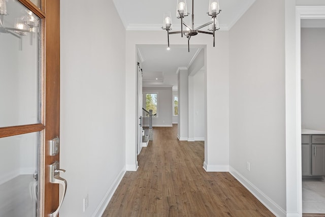 hall with light wood-style flooring, a barn door, ornamental molding, baseboards, and stairs