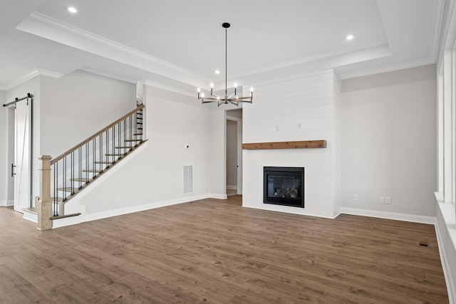 unfurnished living room with hardwood / wood-style flooring, an inviting chandelier, ornamental molding, a large fireplace, and a barn door