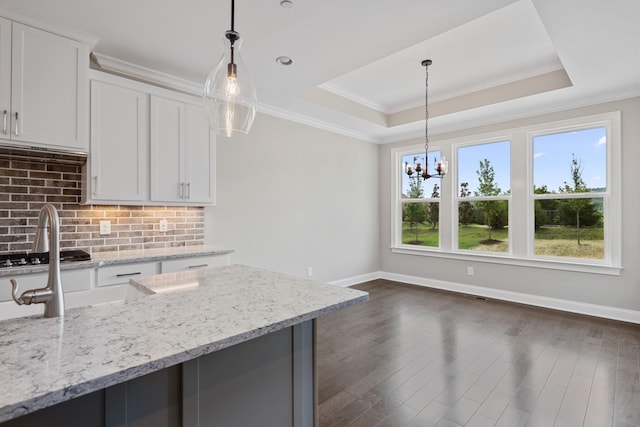 kitchen featuring white cabinetry, light stone countertops, pendant lighting, and a tray ceiling