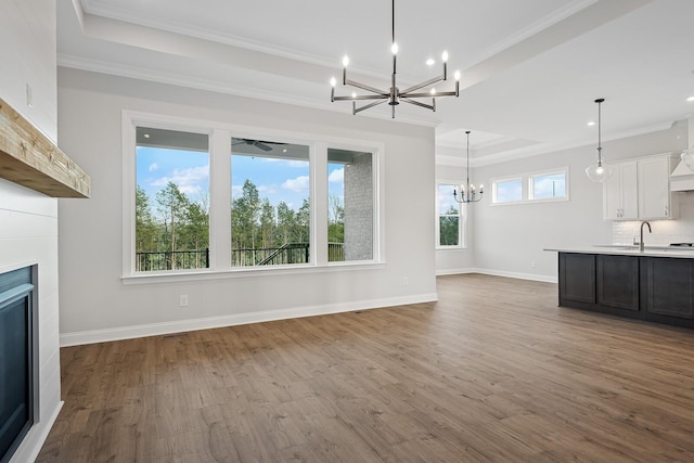 unfurnished living room featuring sink, crown molding, a tray ceiling, a notable chandelier, and hardwood / wood-style flooring