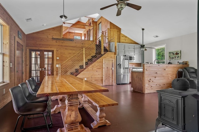 dining area with french doors, wood walls, high vaulted ceiling, a wood stove, and ceiling fan