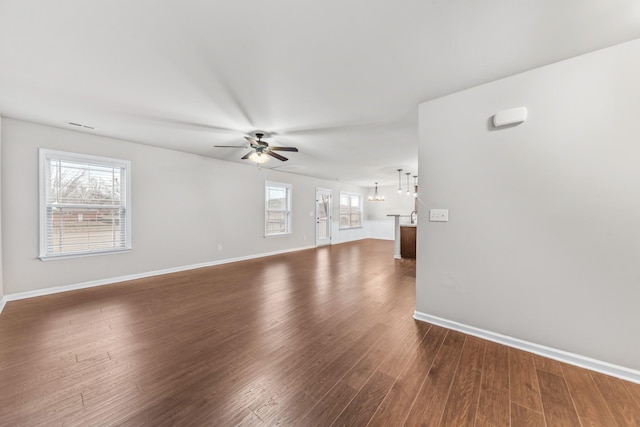 unfurnished living room with ceiling fan with notable chandelier, a wealth of natural light, and dark hardwood / wood-style floors