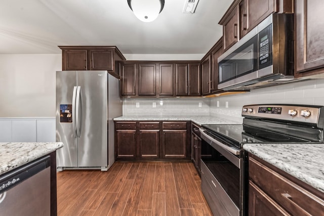 kitchen featuring backsplash, dark brown cabinetry, light stone counters, stainless steel appliances, and dark wood-type flooring