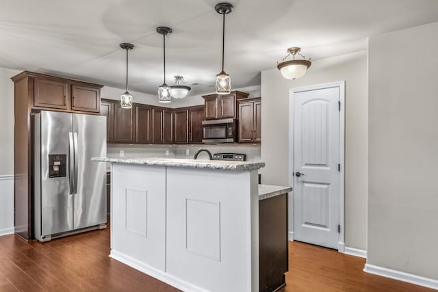 kitchen with light stone counters, dark brown cabinets, appliances with stainless steel finishes, and hanging light fixtures