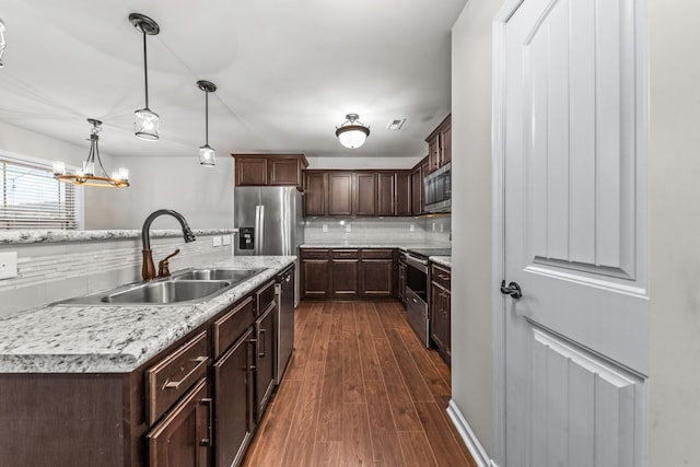 kitchen featuring sink, decorative light fixtures, appliances with stainless steel finishes, dark hardwood / wood-style flooring, and an island with sink