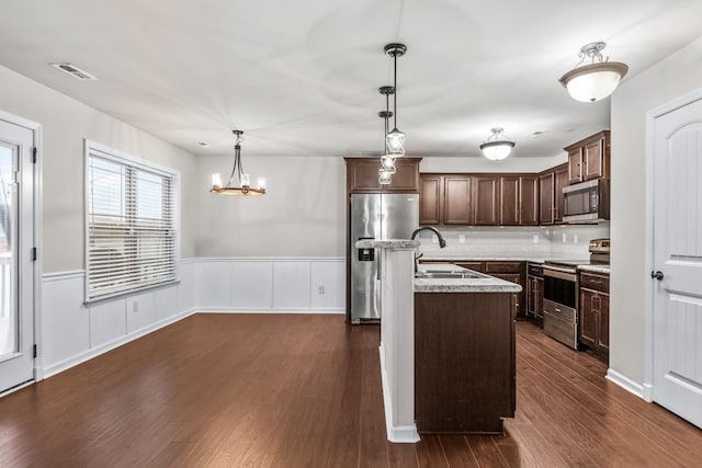 kitchen featuring appliances with stainless steel finishes, sink, hanging light fixtures, a kitchen island with sink, and dark brown cabinetry