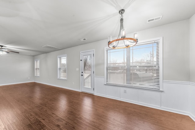 empty room with dark hardwood / wood-style flooring and ceiling fan with notable chandelier