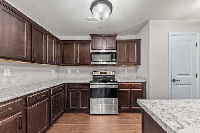 kitchen with stainless steel appliances, light stone countertops, dark wood-type flooring, and dark brown cabinetry