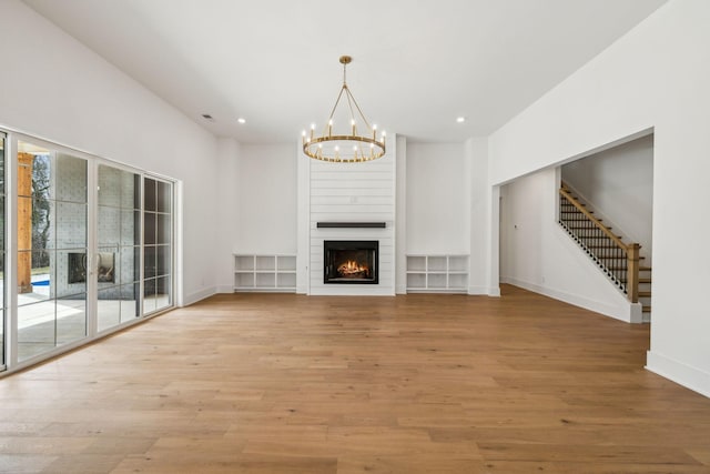 unfurnished living room with an inviting chandelier, a fireplace, and light hardwood / wood-style floors