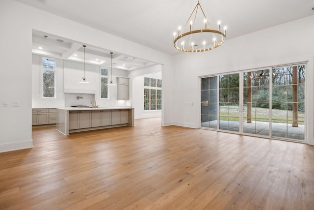 unfurnished living room with sink, a notable chandelier, and light hardwood / wood-style floors