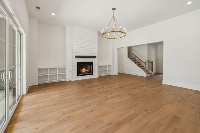 unfurnished living room featuring a large fireplace, a chandelier, and light wood-type flooring