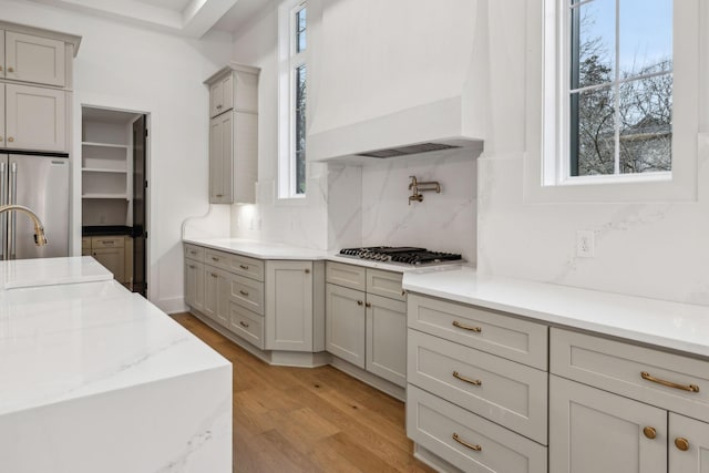 kitchen featuring gray cabinets, appliances with stainless steel finishes, decorative backsplash, custom exhaust hood, and light wood-type flooring