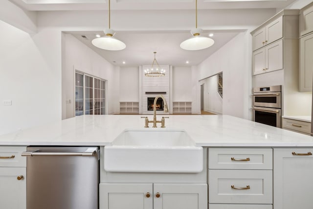 kitchen with light stone counters, appliances with stainless steel finishes, sink, and hanging light fixtures