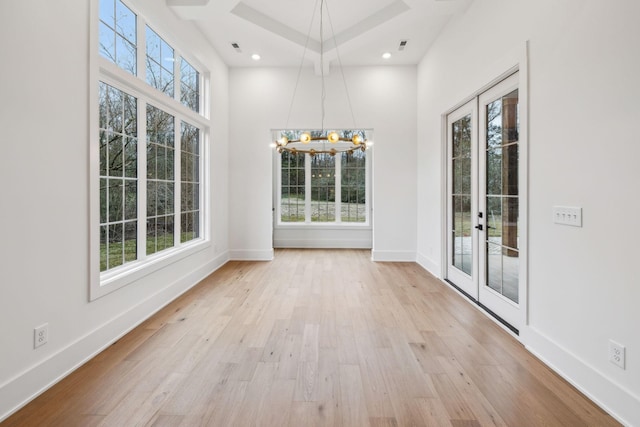 unfurnished dining area with an inviting chandelier, light hardwood / wood-style flooring, and french doors