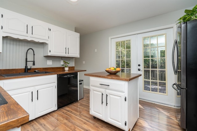 kitchen with butcher block counters, black dishwasher, white cabinets, sink, and stainless steel fridge