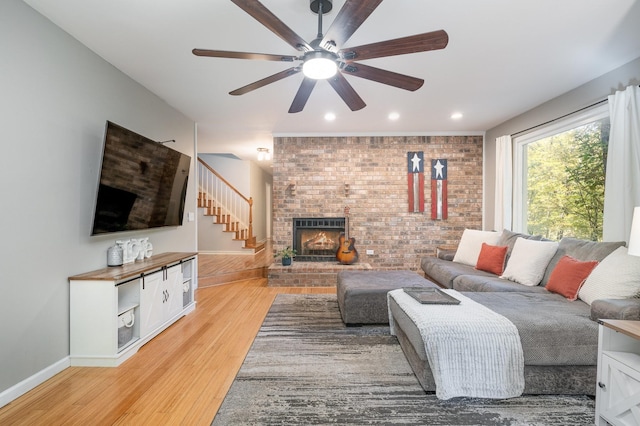 living room featuring ceiling fan, brick wall, a fireplace, and light hardwood / wood-style flooring